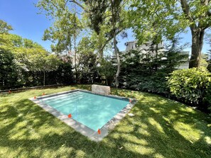 Una piscina rectangular rodeada de césped y árboles cuidados, con un muro de ladrillo y banderas naranjas que marcan el borde de la piscina.