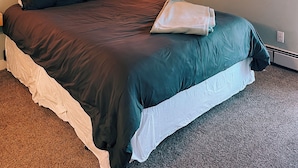 A bedroom with a bed, wooden headboard, a wall-mounted light fixture, and a nightstand.