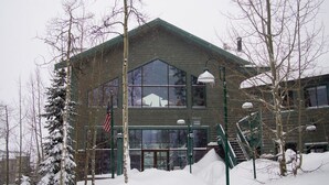 A two-story building with large windows and a green roof, surrounded by snow-covered trees.