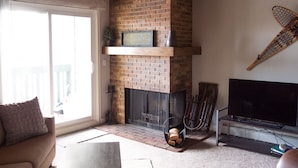 A living room with a brick fireplace, a television, and a sliding glass door leading to a balcony.