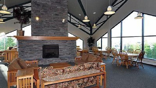 A spacious indoor area with a stone fireplace, wooden furniture, and large windows allowing natural light.