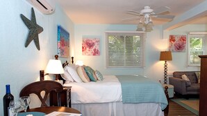 A bedroom with a bed, a desk with a lamp, a starfish decoration, and a ceiling fan. - THE COTTAGE - 32 Steps to the Beach - Sleeps 2, drive to your door, Wifi, Grill. (Clearwater)
