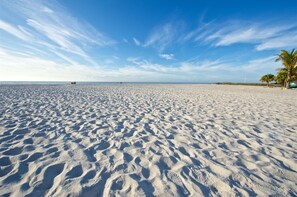 A wide sandy beach with footprints, palm trees, and a distant red boat. - THE COTTAGE - 32 Steps to the Beach - Sleeps 2, drive to your door, Wifi, Grill. (Clearwater)