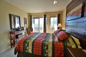 A bedroom with a large bed, a dresser, a television, and a window with curtains.