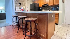 Eine Küche mit Holzausstattung, einem schwarzen Kühlschrank, einer Mikrowelle und einer Arbeitsplatte mit Spüle und Barhocker.