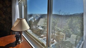 Eine Lampe auf einem Holztisch neben einem Fenster mit Blick auf eine verschneite Landschaft.