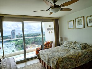 A bedroom with a large window, a ceiling fan, and a bed with patterned bedding.