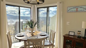 A dining area with a round table set for four, large windows offering a view of the sky and landscape, a chandelier, and a sign indicating the hotel's location. - AUGUST DISCOUNT DAYS BEST VIEWS@BERNARDS LANDING- BOOK NOW (Moneta)