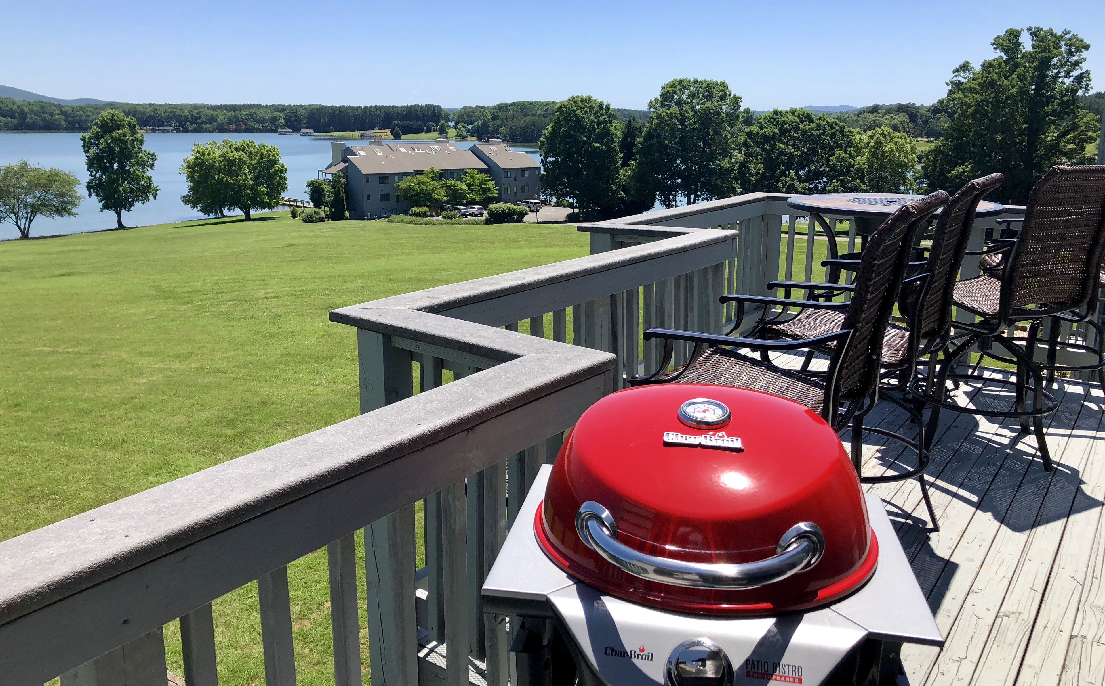 Une terrasse équipée d’un barbecue Char-Broil, de mobilier d’extérieur et offrant une vue sur un lac et des bâtiments.