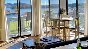 A room with a large sliding glass door leading to a balcony with a view of a lake and mountains. There is a dining table with chairs, a sofa, and a coffee table. - AUGUST DISCOUNT DAYS BEST VIEWS@BERNARDS LANDING- BOOK NOW (Moneta)