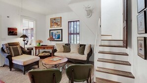 A spacious living room with a high ceiling, a staircase, and a mounted deer head on the wall. - Authentic German Sunday House! Location, Outdoor Fireplace & Upscale Decor! (Fredericksburg)