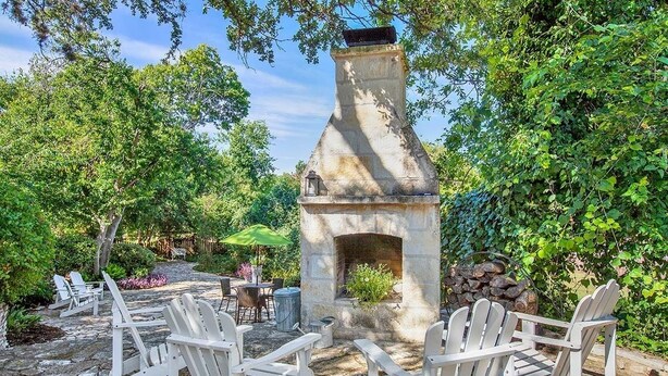 A stone fireplace surrounded by Adirondack chairs in a garden setting. - Authentic German Sunday House! Location, Outdoor Fireplace & Upscale Decor! (Fredericksburg)