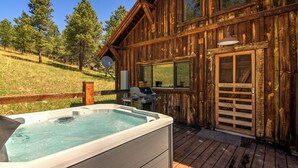 Una cabaña de madera con jacuzzi, parrilla exterior y terraza.