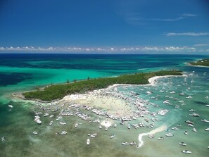 Vista aérea de una playa con numerosas embarcaciones ancladas en el agua y una gran multitud de personas en la arena.