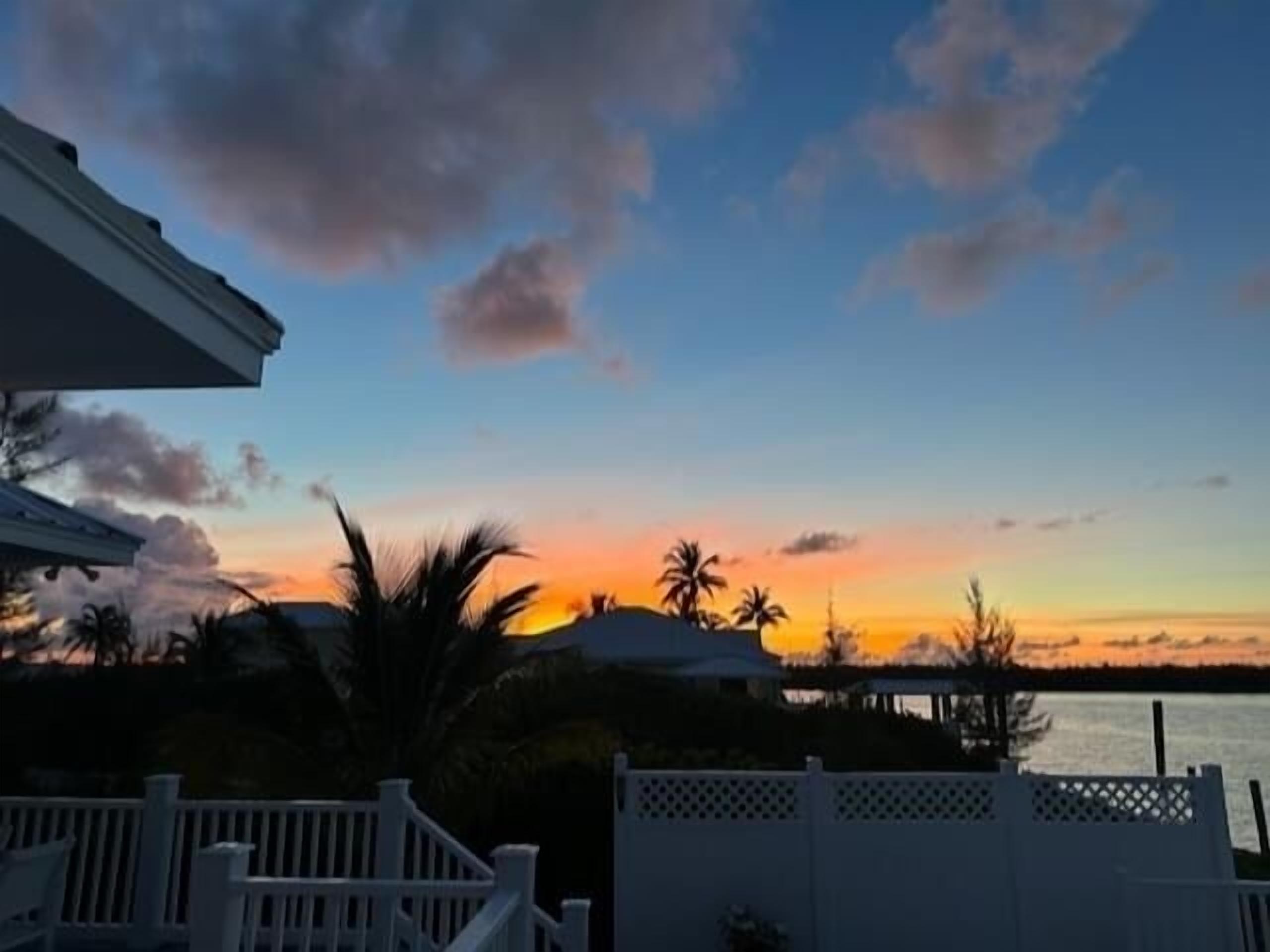 A sunset view from a balcony with a white fence and palm trees.