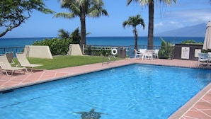 En swimmingpool med en livräddarstol, solstolar och utsikt över havet.