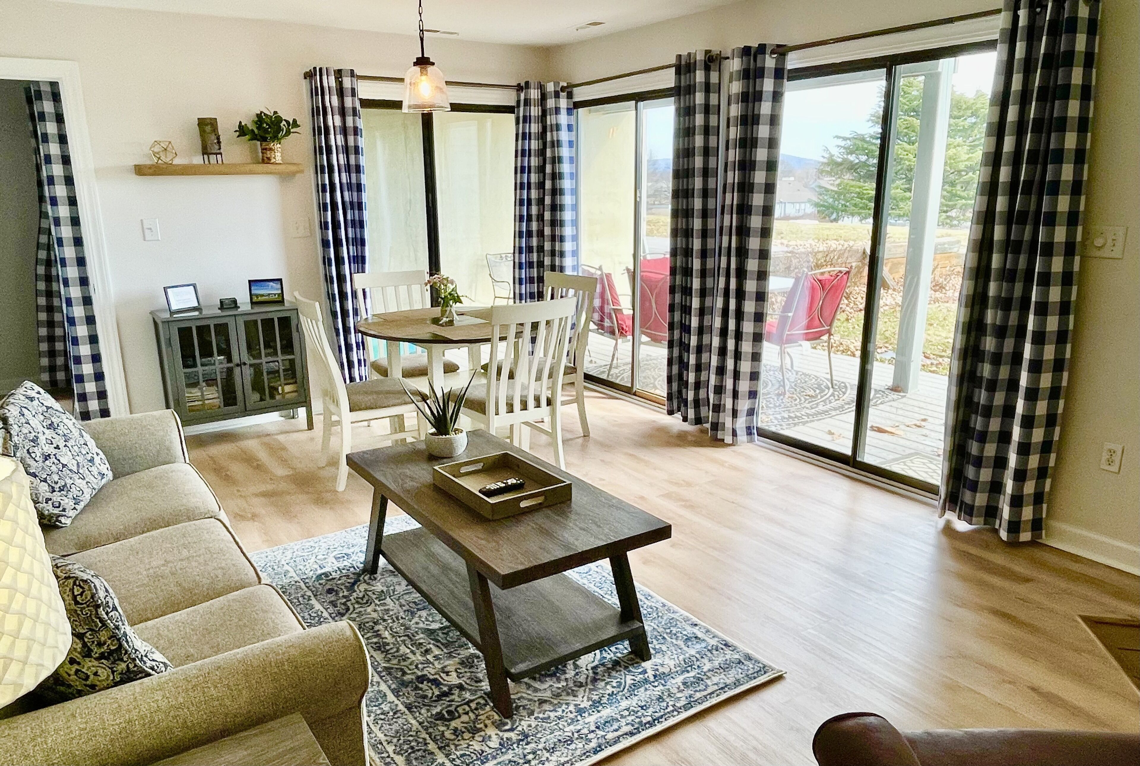 A spacious living area with a sofa, a coffee table, and a dining table. There is a sliding glass door leading to an outdoor patio.