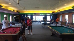 Une salle de billard avec plusieurs tables de billard, un jeu de fléchettes et un drapeau.