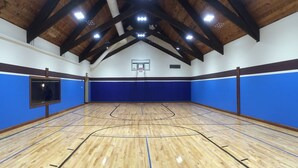 Un terrain de basket-ball intérieur doté d’un plancher en bois, d’un panier de basket et de murs bleus rembourrés.