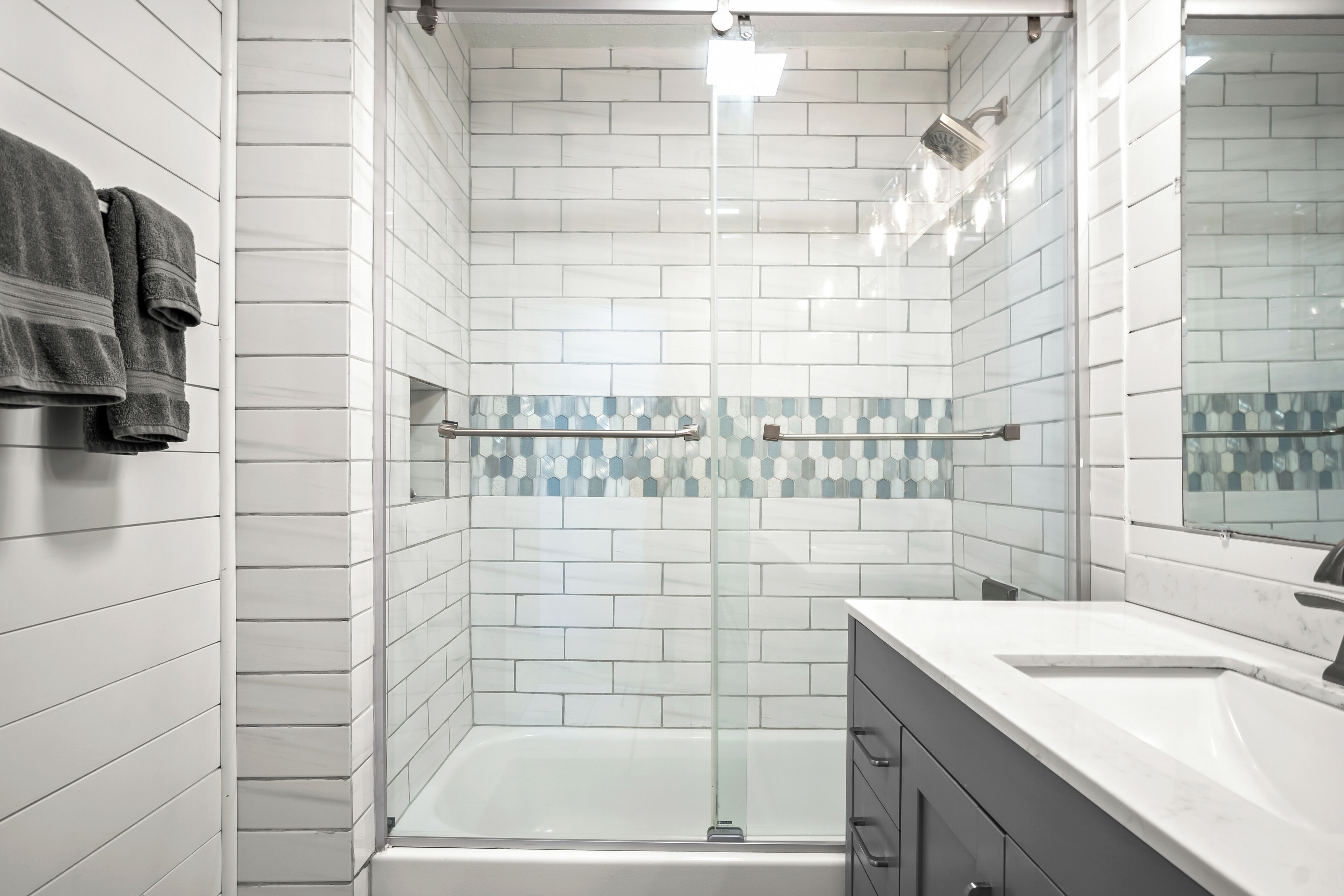 Een moderne badkamer met witte betegelde wanden, een douche met glazen wand, een bad, een wastafelmeubel en een spiegel.