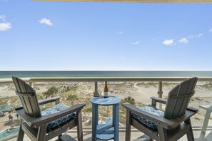 Un balcon avec deux fauteuils Adirondack, une petite table ronde et une bouteille de champagne. La vue comprend une plage et l’océan.