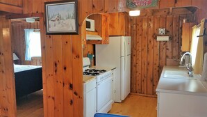 A compact kitchen with wooden walls, a stove, a refrigerator, and a sink.