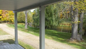 A covered outdoor area with a view of a pond and trees.