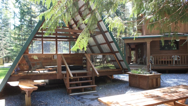 A wooden cabin with a sloped roof, wooden deck, and picnic tables.