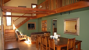 A dining area with a wooden table and chairs, a staircase, and a television in the background.