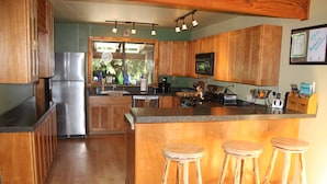 A kitchen with wooden cabinets, a stainless steel refrigerator, a large island with stools, and a view of the outdoors.