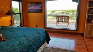 A bedroom with a large bed, a window with a view of a rocky landscape, a wooden bench outside, and a bookshelf. - Chisholm Cabin on the North Rim (Canyon)