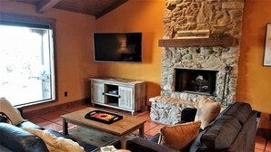 A cozy living room with a stone fireplace, a flat-screen TV mounted above it, and a comfortable seating area with a sofa and armchairs. - Chisholm Cabin on the North Rim (Canyon)