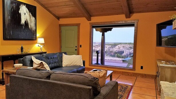 A living room with a sofa, a table with a lamp, a painting, and a large window with a view. - Chisholm Cabin on the North Rim (Canyon)