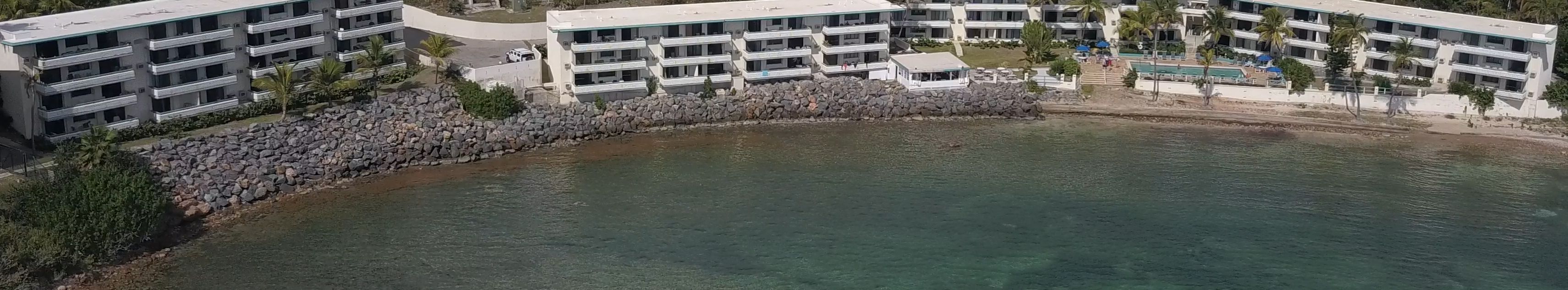 A coastal hotel with multiple buildings, a pool, and a rocky shoreline.