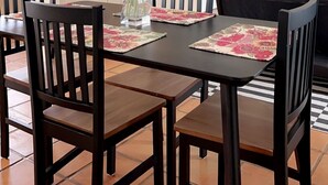 Un coin repas avec une table et des chaises en bois, un vase de fleurs et, au fond, une cuisine.