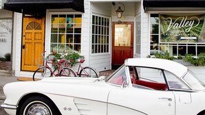 Un coche blanco antiguo estacionado frente a un edificio blanco con un toldo negro y un cartel que dice 'Valley Wine Merchants'.
