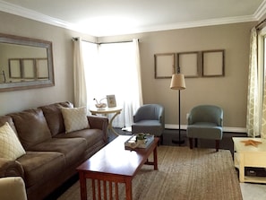 A living room with a brown leather sofa, two armchairs, a wooden coffee table, a floor lamp, and a small side table with a starfish decoration.