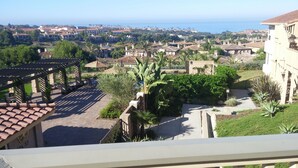 Ein Wohngebiet mit Meerblick, mit Häusern mit roten Ziegeldächern, einer Pergola und einem Garten mit tropischen Pflanzen.