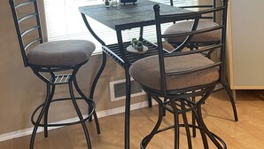 Un coin repas comprenant une table et quatre chaises, une fenêtre avec des stores et une bibliothèque agrémentée d’objets décoratifs.
