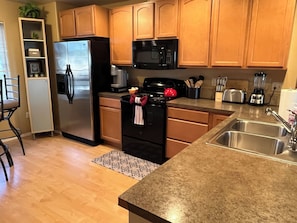 A kitchen with wooden cabinets, a stainless steel refrigerator, a microwave, a stove, and a sink. - From The Mountaintops To The Sea (Port Angeles)