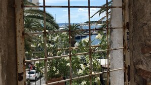 A window with a metal grid, through which a view of palm trees and a building is visible. - Cozy House: first-row beach, ramp accessibility, hottub, AC, gasgrill, W/D prkng (Gradac)