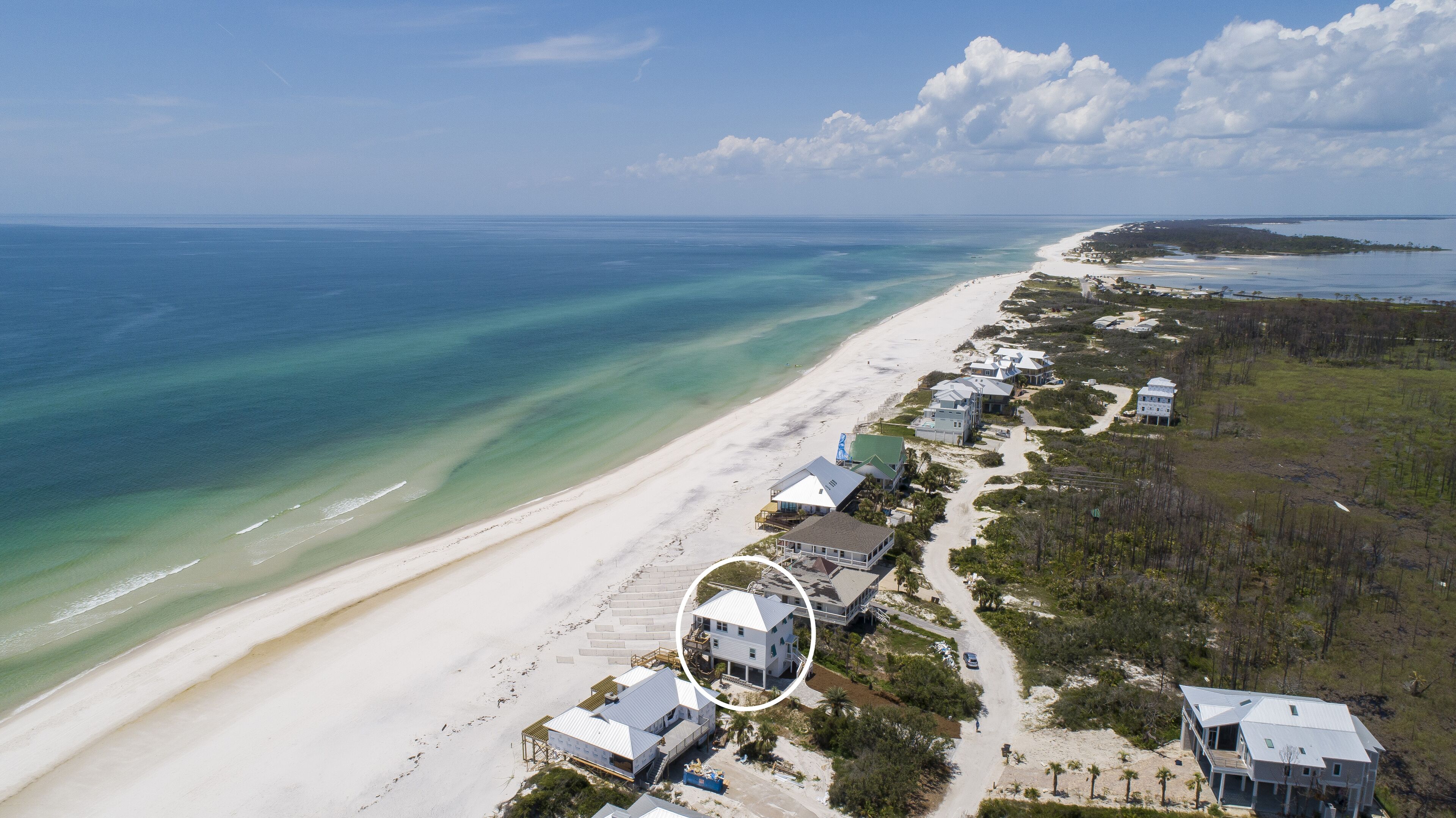 An aerial view of a coastal property with a beach, multiple houses, and a clear view of the ocean.