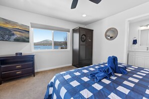 A bedroom with a large bed, a wardrobe, a dresser, a window with a view of a lake, and a painting on the wall. - Modern Lakefront Dream Home, steps to The Village. Spa, Pool Table, Wifi  (Big Bear Lake)