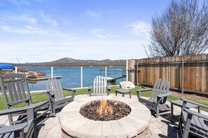 A fire pit surrounded by Adirondack chairs, a wooden fence, and a view of a lake with mountains in the background. - Modern Lakefront Dream Home, steps to The Village. Spa, Pool Table, Wifi  (Big Bear Lake)