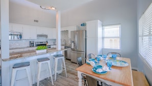 Een moderne keuken met witte kastjes, roestvrijstalen apparatuur en een houten eettafel met blauw servies.