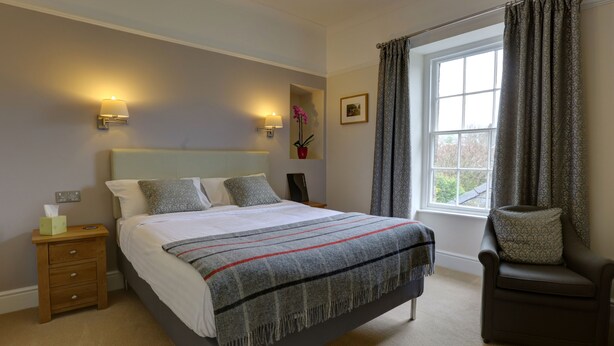 A bedroom with a bed, bedside table, lamp, chair, window, and a wall-mounted picture.