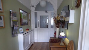 A hallway with a white door, a radiator, a small table with a lamp, and a chair.
