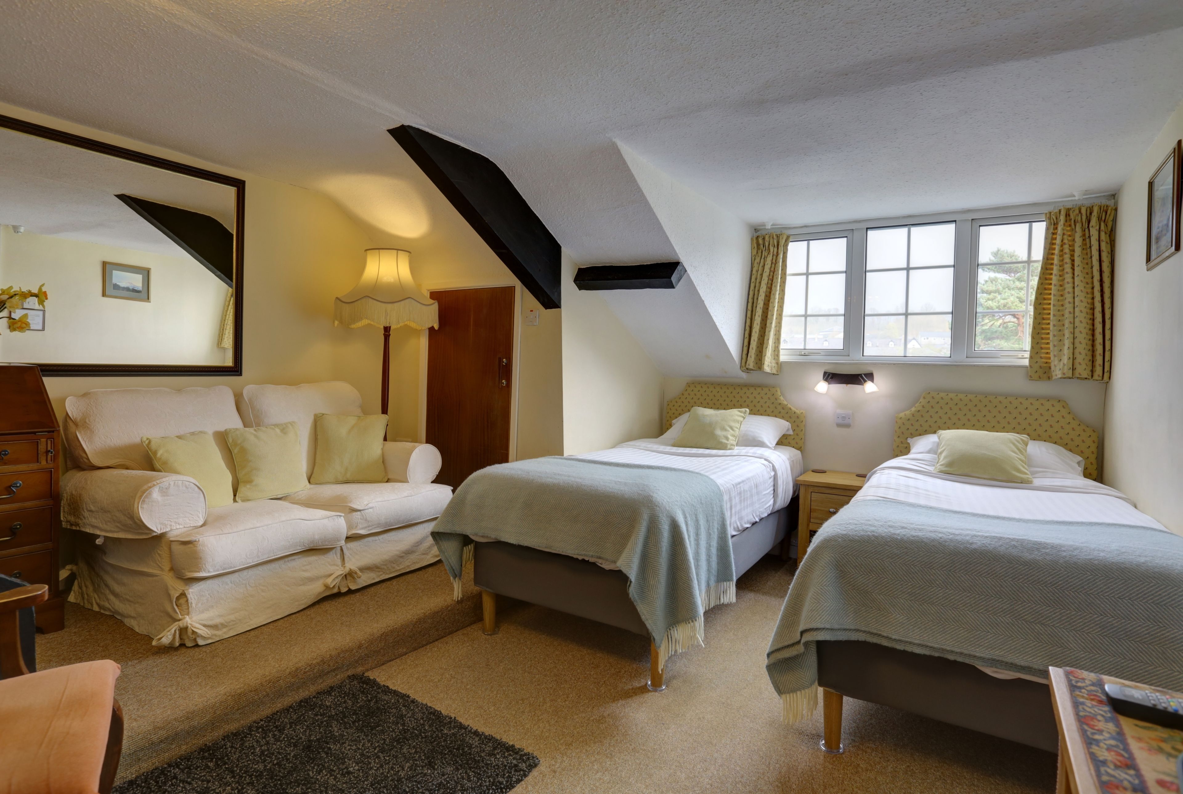A bedroom with two single beds, a sofa, a dresser, and a window with curtains.