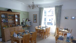 A dining area with wooden furniture, a kitchen area with shelves, and a view through a window.