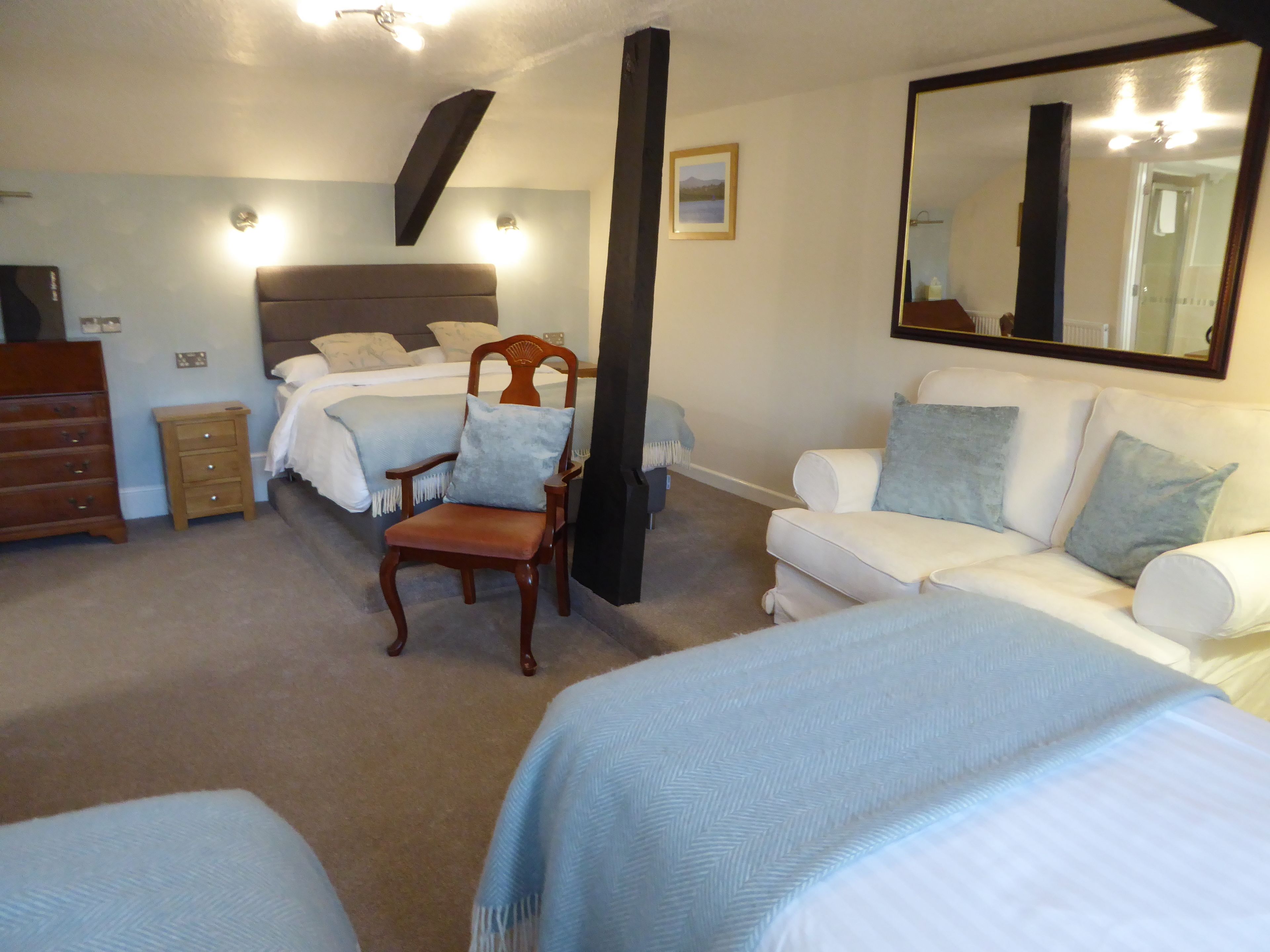 A hotel room with a bed, a chair, a sofa, a dresser, and a large mirror.